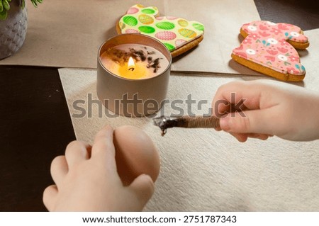 Child decorating Easter egg using traditional wax technique with candle and tool