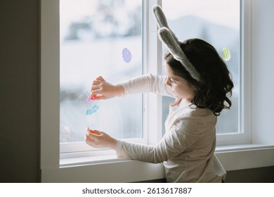 Child decorating window with Easter stickers and eggs.