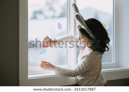 Child decorating window with Easter stickers and eggs.