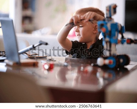 A child is deeply engaged in assembling a robot with a laptop nearby, capturing a moment of focused curiosity and hands-on learning in a modern home setting.