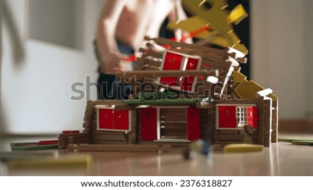 Child destroying house construction miniature. Kid kicking model wood home. Little boy boy misbehavior, educational childhood concept