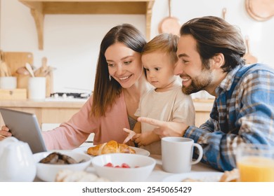 Child developing cartoons video. Caucasian happy parents watching animated movies, having videocall with grandparents on tablet with kid child toddler infant at home kitchen - Powered by Shutterstock