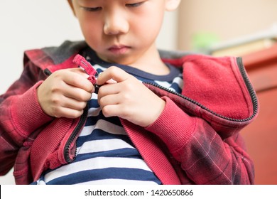 Child Development concept: Close up of a little preschool boy learning to get dressed, zipping his striped red hoodie. Montessori practical life skills - Care of self, Early education from daily life.