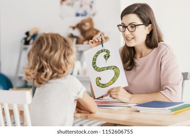 A Child With Development Problems With A Professional Speech Therapist During A Meeting. Tutor Holding A Prop Poster Of A Snake As A Letter 's'.