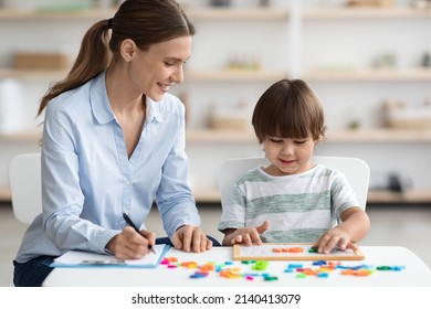 Child Development School. Professional woman language teacher exercising with preschooler, happy little boy making word with colorful letters on table, free space