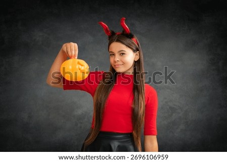 Child with devil horns hold pumpkin. Halloween witch girl. Little girl witch. Kid witch celebrates Halloween. Happy Halloween. Portrait of an Halloween child teen girl.