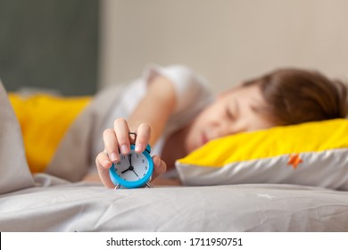 Child Do Not Want To Wake Up In The Morning And He Want Hand Turning Off The Alarm Clock. Kid Trying To Sleep, When Alarm Clock Ringing.