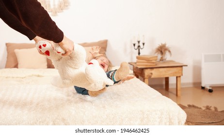 The Child Does Not Want To Share Toys, Cries Screaming Hysterical. A Two-year-old Girl Doesn't Give A Toy Bear. Dad Picks Up A Soft Toy. Beige Home Interior.