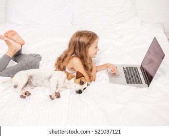 Child And Dog With Laptop. Girl With Computers On Bed. Baby Playing 