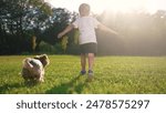 Child and dog is running on the grass. Happy pet fun concept. A dog is running around in a park with kids. A kid and a child are running on the grass near lifestyle a dog.