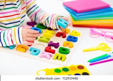 Child doing homework for school at white desk. Wooden educational abc toy puzzle for kids. Happy back to school student. Kid learning alphabet letters. Little girl with school supplies and books.
