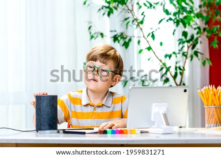 Child doing homework and using smart speaker and voice assistant. Education programme for child. Boy talking to Alexa and give it orders and commands what to switch on. Online lesson.