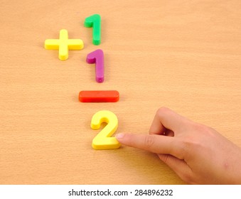 Child doing a sum with plastic items on the school wood desk