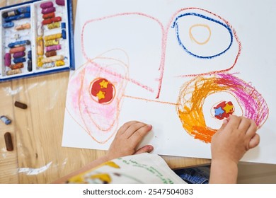 Child drawing with colorful pastels on paper, creating abstract shapes and adding stickers. Art supplies and creative work on a wooden table - Powered by Shutterstock