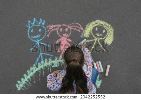 Child drawing family with chalk on asphalt, top view
