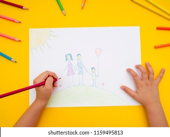 Child drawing family on a paper on vibrant yellow background. Directly above