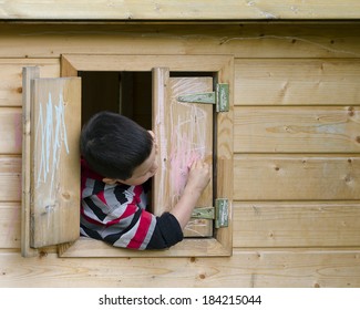 Child Drawing On A Window Shutter Of A Playhouse With A Chalk. 