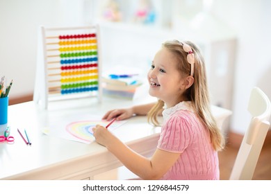 Child drawing rainbow. Kid painting at home. Little girl doing homework after school. Kids desk with abacus in white sunny bedroom. Children study, learn to read and write. Bedroom for young student. - Shutterstock ID 1296844579