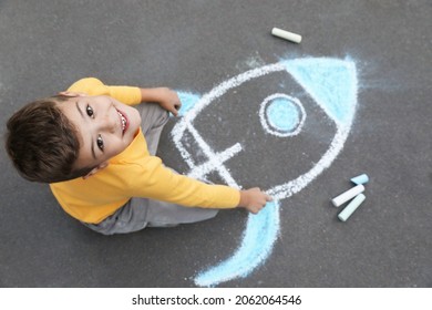 Child Drawing Rocket With Chalk On Asphalt, Above View