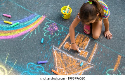 The child draws a house and a rainbow on the asphalt with chalk. Selective focus. Kids. - Powered by Shutterstock