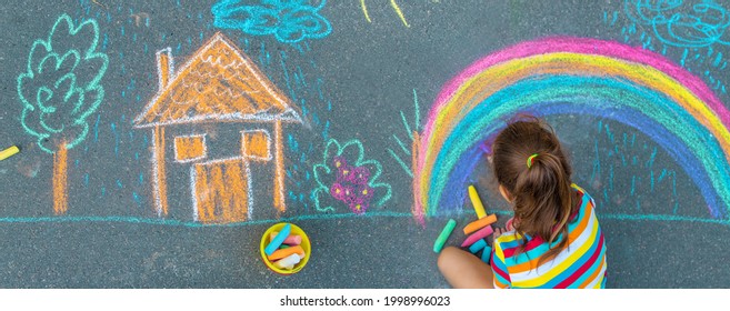 The Child Draws A House And A Rainbow On The Asphalt With Chalk. Selective Focus. Kids.