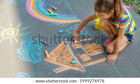 The child draws a house and a rainbow on the asphalt with chalk. Selective focus. Kids.