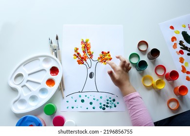 A child draws leafs on a tree. Ideas for drawing with finger paints. Finger painting for kids on white background. Little girl painting by finger hand paint color. Children development concept.