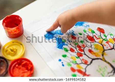 A child draws leafs on a tree. Ideas for drawing with finger paints. Finger painting for kids on white background. Little girl painting by finger hand paint color. Children development concept. 