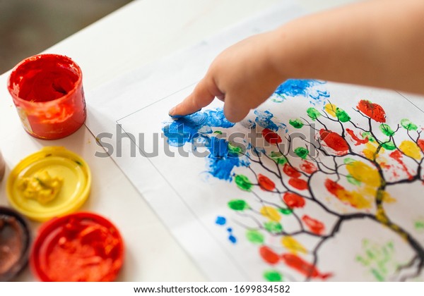 A child draws leafs on a tree. Ideas for drawing with\
finger paints. Finger painting for kids on white background. Little\
girl painting by finger hand paint color. Children development\
concept. 