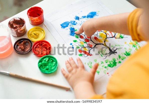 A child draws leafs on a tree. Ideas for drawing with
finger paints. Finger painting for kids on white background. Little
girl painting by finger hand paint color. Children development
concept. 