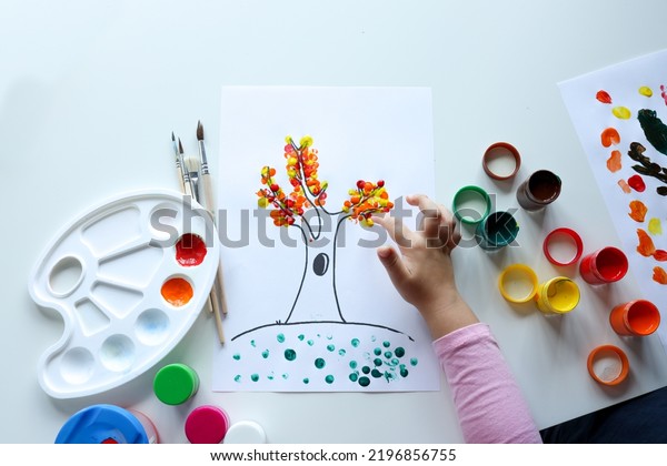 A child draws leafs on a tree. Ideas for drawing\
with finger paints. Finger painting for kids on white background.\
Little girl painting by finger hand paint color. Children\
development concept.