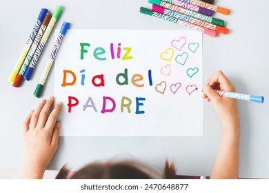 child draws with multi-colored felt-tip pens a poster gift card for dad for the holiday Father's Day with the inscription Happy Fathers's Day in Spanish, holiday concept. - Powered by Shutterstock