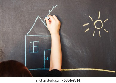 child draws on blackboard chalk house