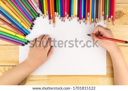 the child draws and a lot of pencils and paints for drawing on a wooden background