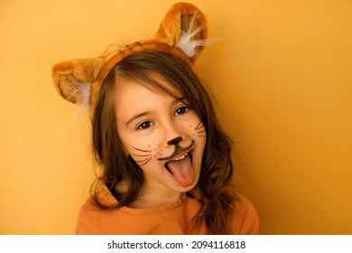 A child dressed up as a tiger with a painted mustache and a hat with ears growls and shows his tongue. Funny cute beautiful girl in the image. lunar cycle of the Chinese animal zodiac. New year 2022