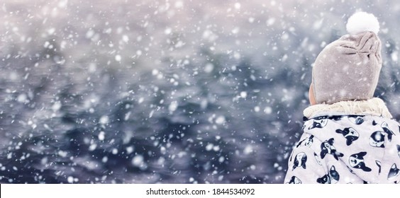 A child dressed in winter clothes watches shiny snow flakes falling like feathers with fascination and joy about wintertime. Copy space, background or horizontal banner for an advertisement. No face