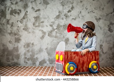 Child Driving A Car Made Of Cardboard Box. Kid Having Fun At Home. Child Shouting Vintage Megaphone. Kid Playing Indoors. Travel And Summer Vacation Concept. Imagination And Freedom Concept