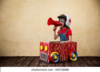 Child Driving A Car Made Of Cardboard Box. Kid Having Fun At Home. Travel And Summer Vacation Concept