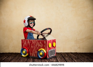 Child Driving A Car Made Of Cardboard Box. Kid Having Fun At Home. Travel And Summer Vacation Concept