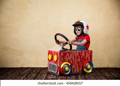 Child driving a car made of cardboard box. Kid having fun indoors. Child playing at home. Dream, imagination, childhood. Travel and summer vacation concept