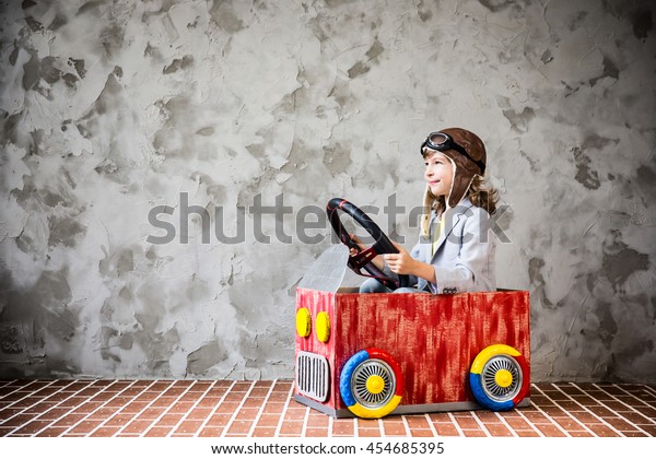Child driving a car made of\
cardboard box. Kid having fun at home. Travel and vacation\
concept