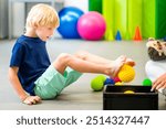 Child during physical therapy session. Boy exercising barefoot with textured surface ball in physio therapy. Flat feet.