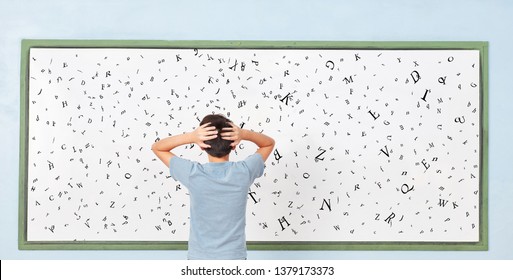 Child With Dyslexia Is Standing In Front Of A Blackboard With Many Letters At School