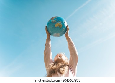Child with Earth Globe. Portrait of a blonde European girl of elementary school with an educational globe of the planet Earth in nature in sunny weather. Study, education, conservation and