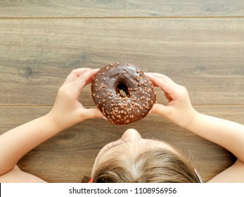 The Child Eating Donut On Rustic Wooden Background. Top View With Copy Space Above.