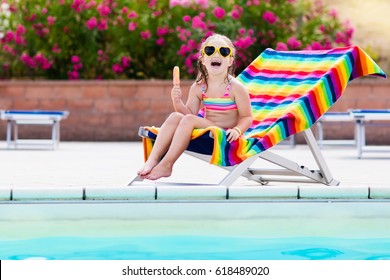 Child Eating Ice Cream At Swimming Pool. Little Girl Relaxing In Colorful Chair At Outdoor Pool Of Exotic Tropical Resort During Family Summer Beach Vacation. Kids Swim And Eat Healthy Snack