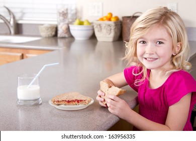 Child eating a peanut butter and jelly sandwich sitting at table in kitchen at home