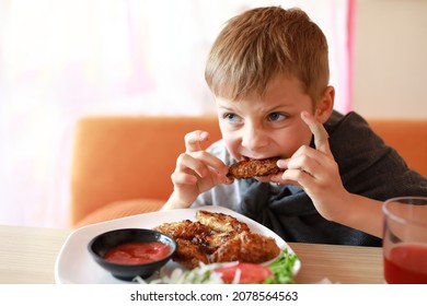 Child Eating Roasted Chicken Wings In Restaurant