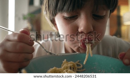 Child eating spaghetti noddles furing mealtime, close-up face of 5 year old little boy enjoying carb rich food