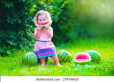 Child Eating Watermelon In The Garden. Kids Eat Fruit Outdoors. Healthy Snack For Children. Little Girl Playing In The Garden Holding A Slice Of Water Melon. Kid Gardening.